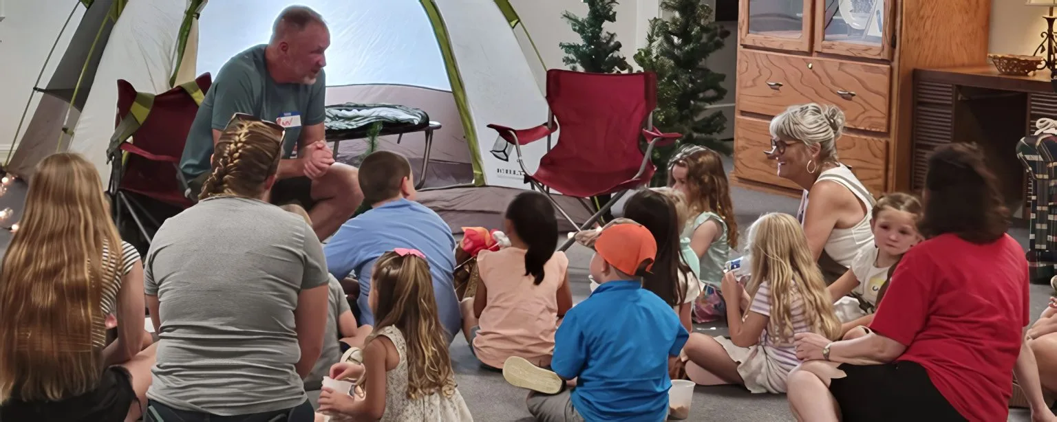 Group of children and adults sitting on the floor listening to a teacher